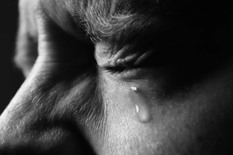 A close-up, black and white shot of a person's eye with a tear rolling down their cheek.