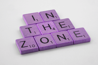 A set of Scrabble tiles spelling out the word "in the zone" on purple wooden blocks 