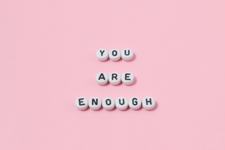 White letter beads spell out "YOU ARE ENOUGH" on a pink background.