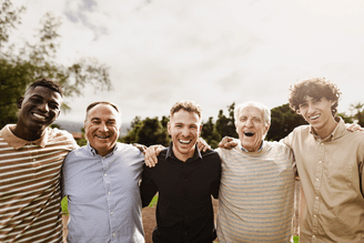 A group of five men with their arms around each other's shoulders, smiling at the camera outdoors.