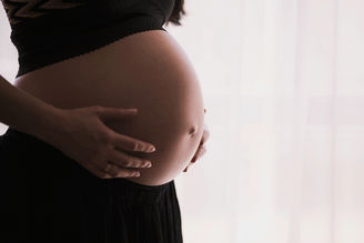 A pregnant person wearing a black top and skirt, cradling their belly with both hands.