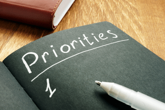A notebook with the word Priorities written on a page, with the number 1 below it and a pen resting on the page.