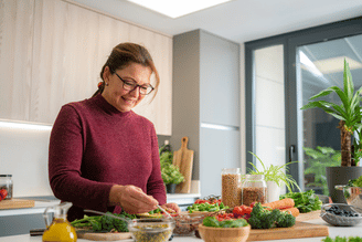 A person in a burgundy sweater preparing fresh vegetables in a modern kitchen with ingredients laid out on the counter.