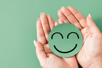 Cupped hands gently hold a green circle with a smiling face drawn in black lines.