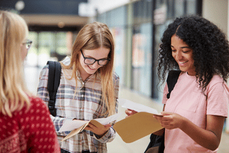 Three students looking at exam results papers in a school hallway.
