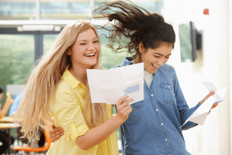 Two laughing students holding letters, one with blonde hair in a yellow shirt and another with dark hair in a blue denim shirt.