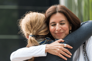 A woman hugs a daughter   smiling warmly while holding the child close in an outdoor setting.