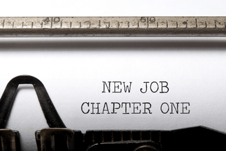 Close-up of an open typewriter with the words “NEW JOB” and “CHAPTER ONE” typed on a white sheet.