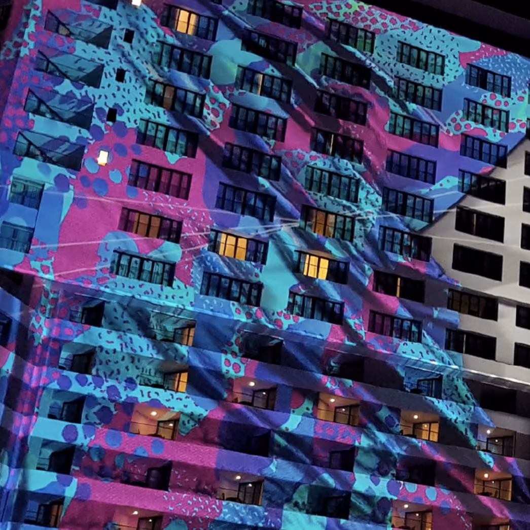 Residential tower facade covered in magenta and turquoise projection mapping at night