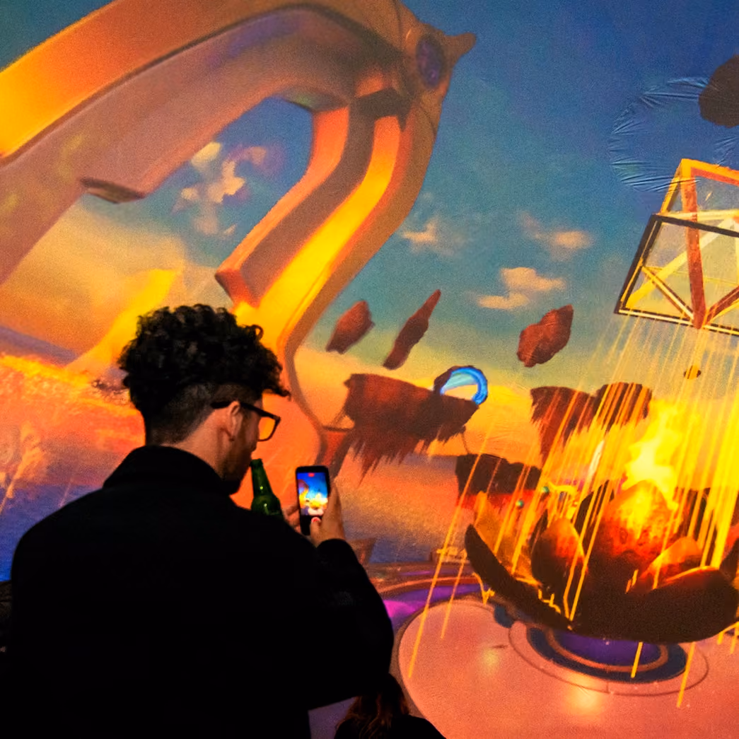 Visitor photographing a large-scale immersive projection of a surreal floating landscape