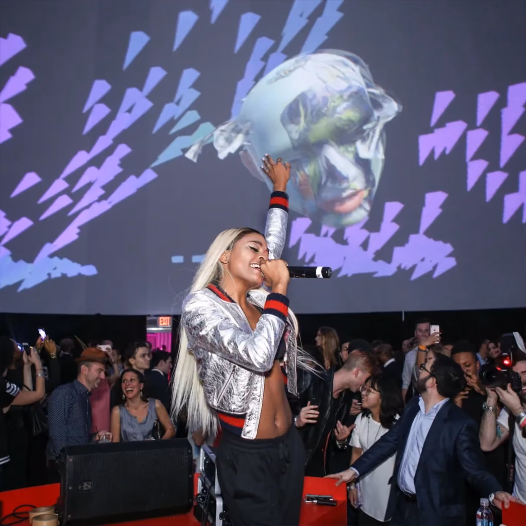 Singer performing with a microphone in front of large-scale projected visuals at a live event