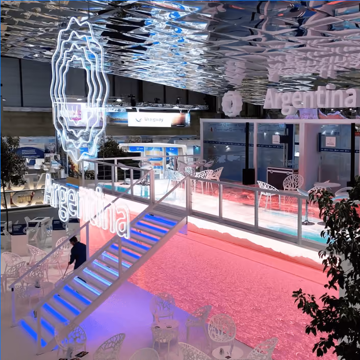 Argentina pavilion at a trade show, with illuminated staircase, neon signage and a sculpted white ceiling