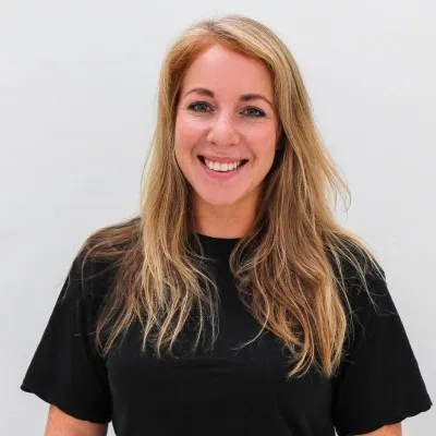 Smiling woman with long blonde hair wearing a black shirt against a plain light background.