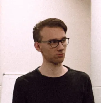 Young man with short brown hair and glasses looking to the side, wearing a black shirt.