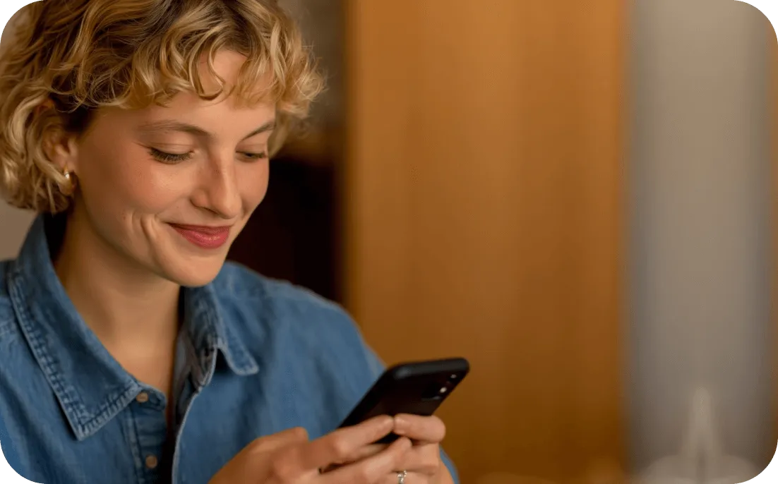 Smiling young woman with short curly hair wearing a denim shirt looking at her smartphone.
