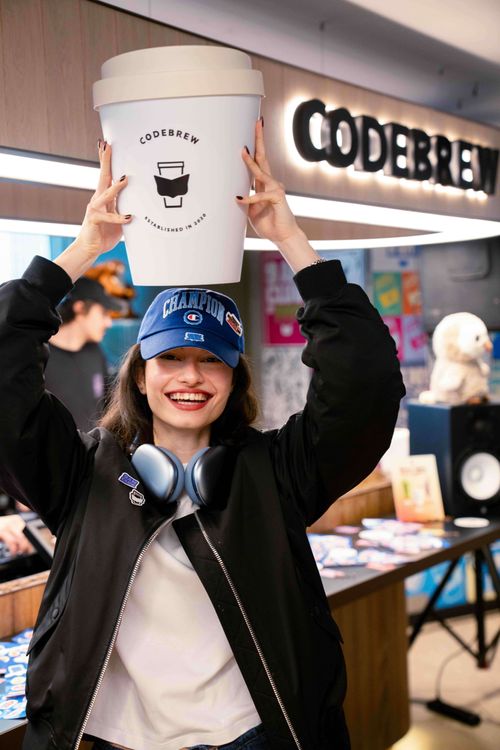 A girl smiling and holding a big coffee cup on her head.