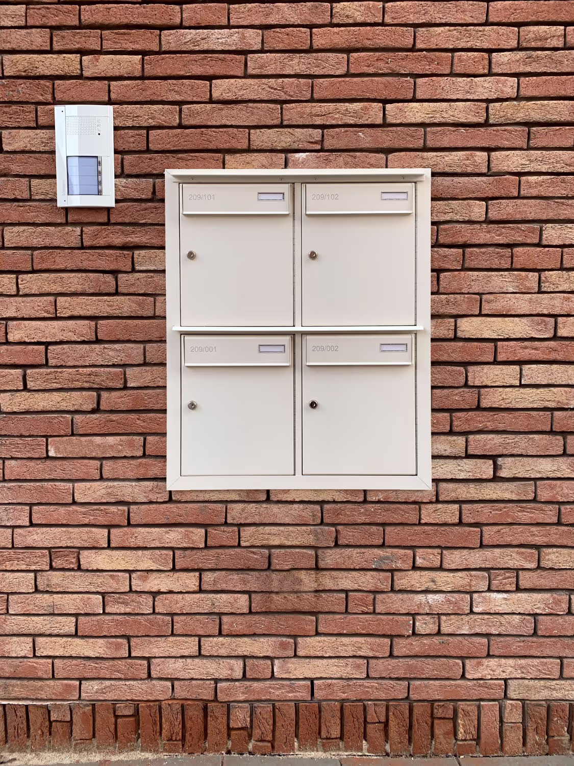 Een wit brievenbusgeheel tegen een bakstenen muur.