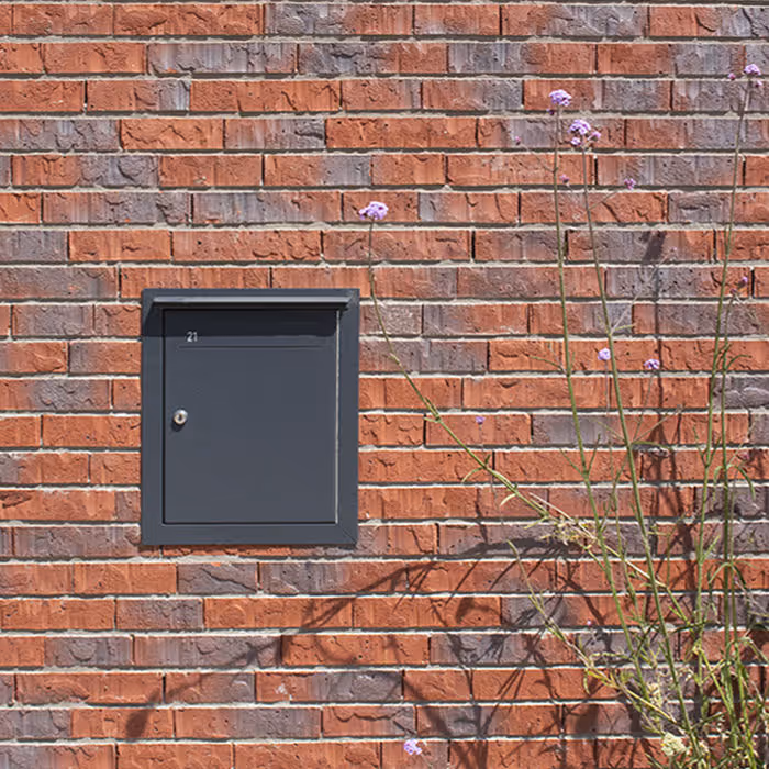 Een zwarte brievenbus in een bakstenen muur verwerkt.