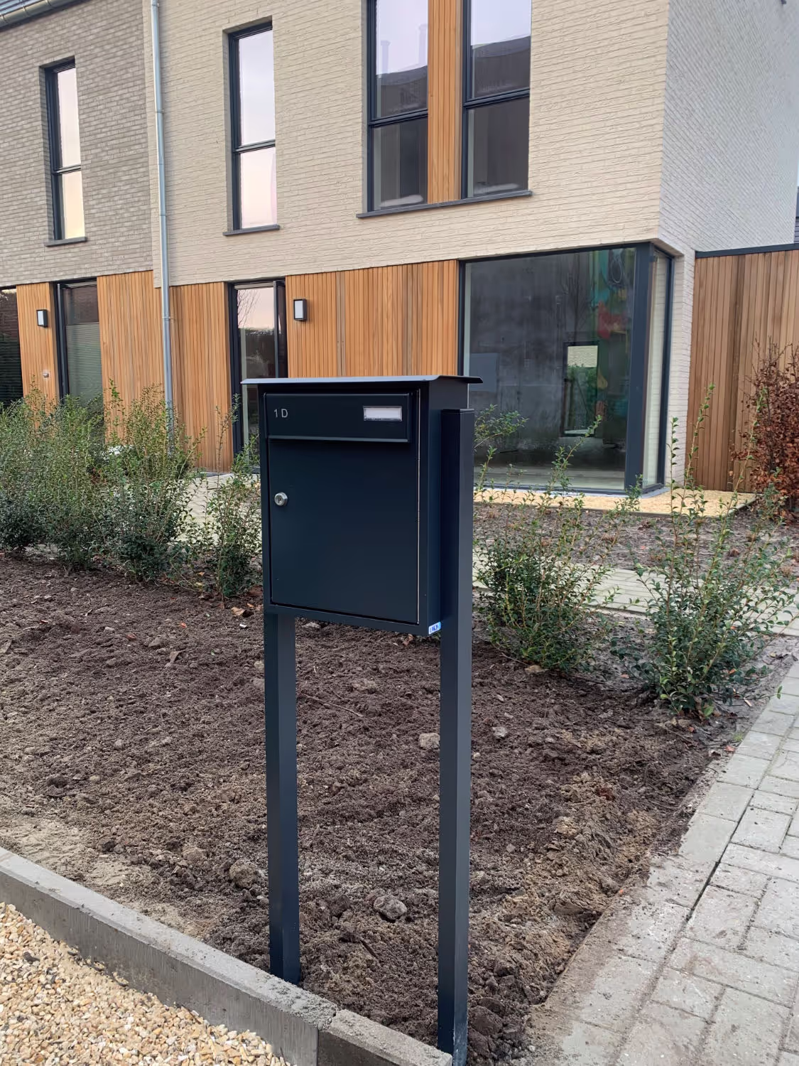 Une boîte aux lettres noire sur pied devant un immeuble.