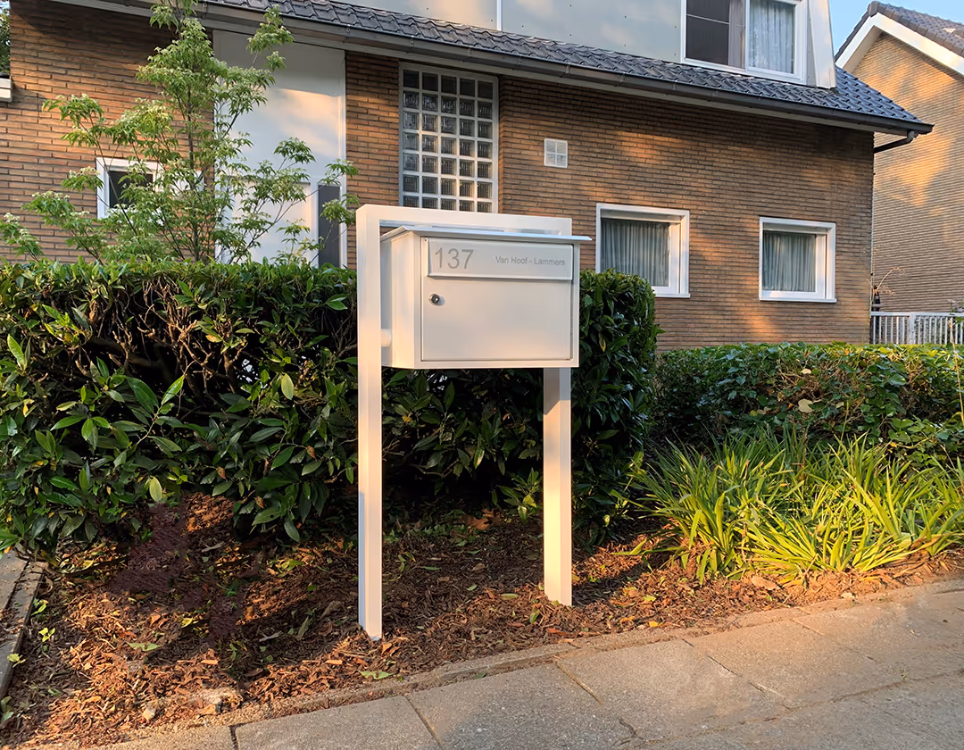 Une boîte aux lettres blanche sur pied devant une maison.