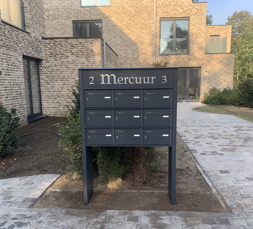 Une boîte aux lettres gris foncé sur pied avec le nom de la résidence.