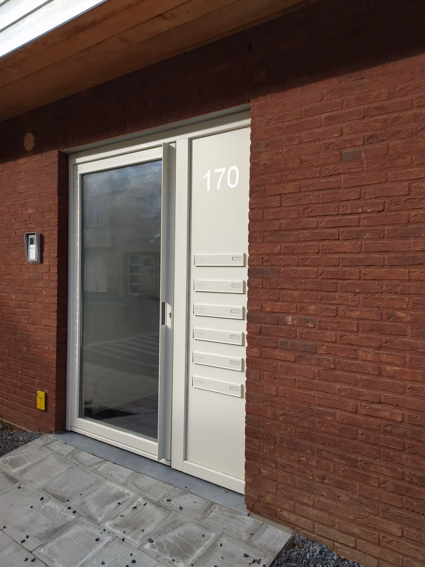 Een glazen deur met witte omkadering, met daarnaast brievenbuskleppen.