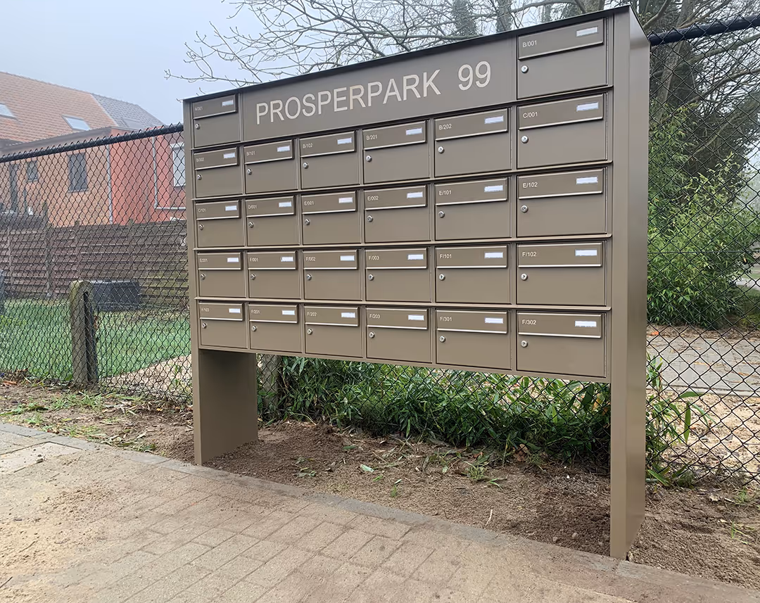 Une grande boîte aux lettres marron sur pied portant le nom de la résidence.