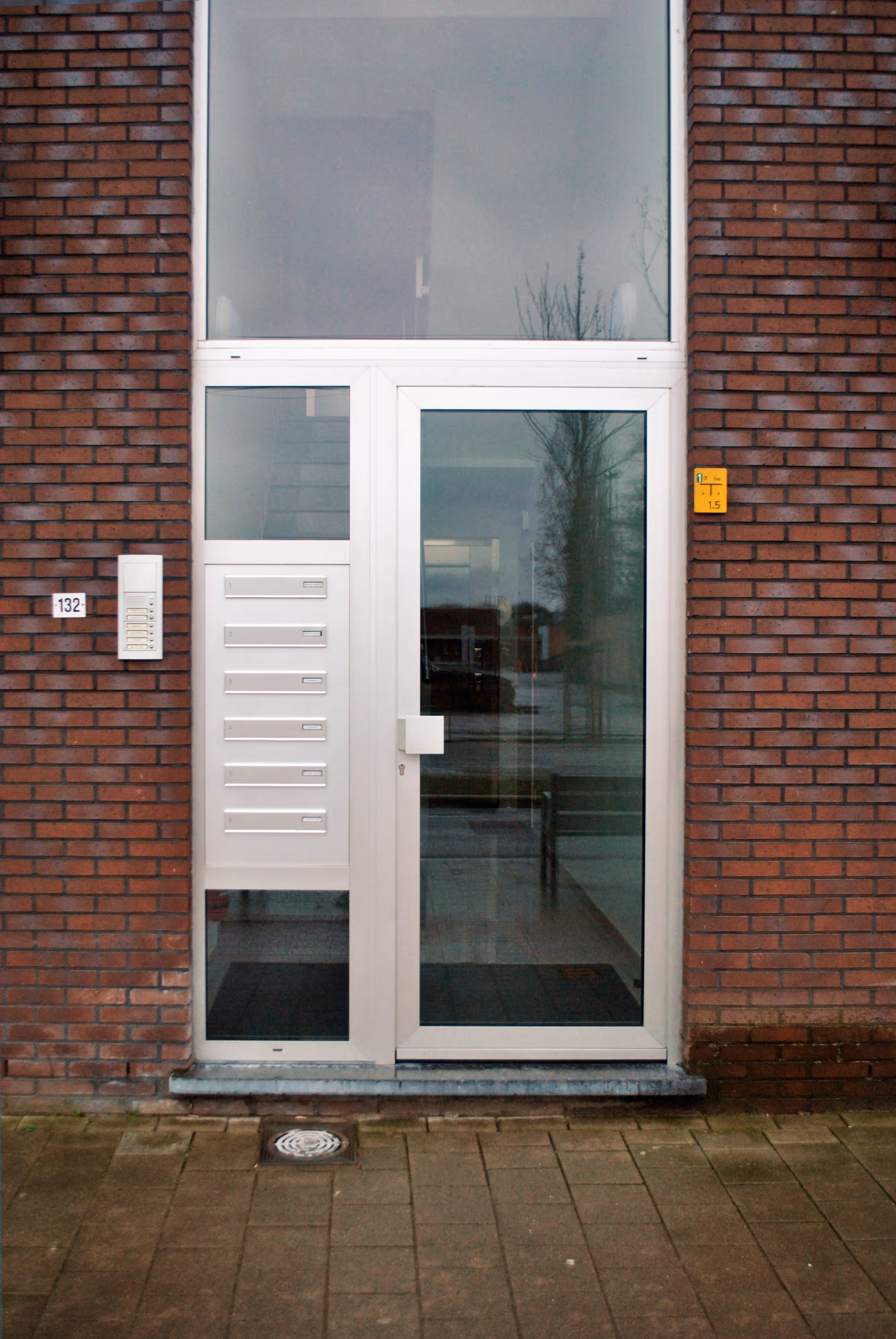 Een glazen deur met witte omkadering met daarnaast een aantal brievenbuskleppen, eveneens in het wit.