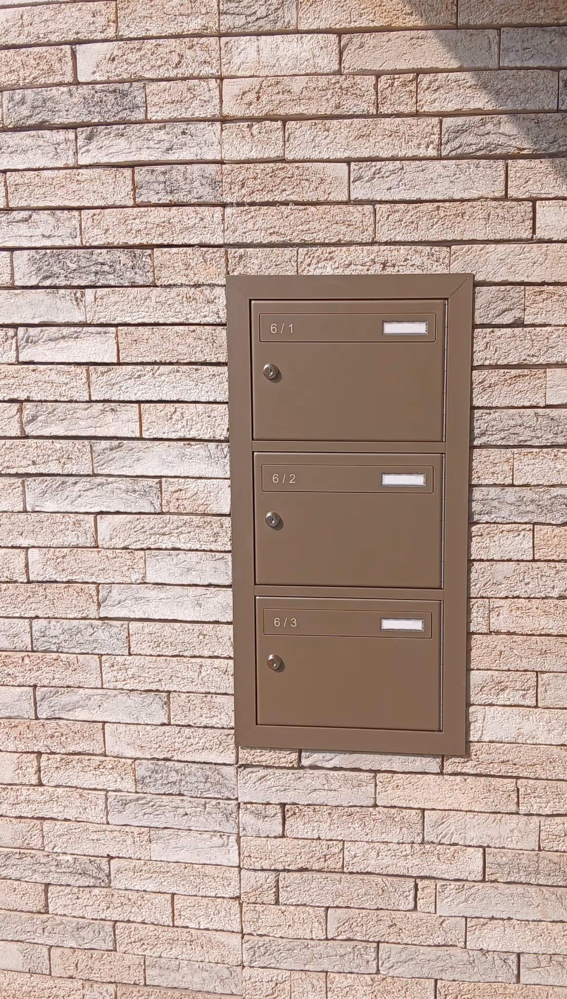 Un ensemble de 3 boîtes aux lettres marron, intégrées dans un mur en briques.