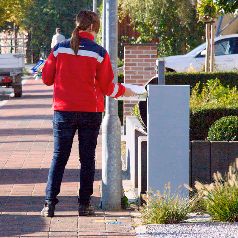 Un facteur déposant un colis dans une boîte aux lettres moderne et grise.