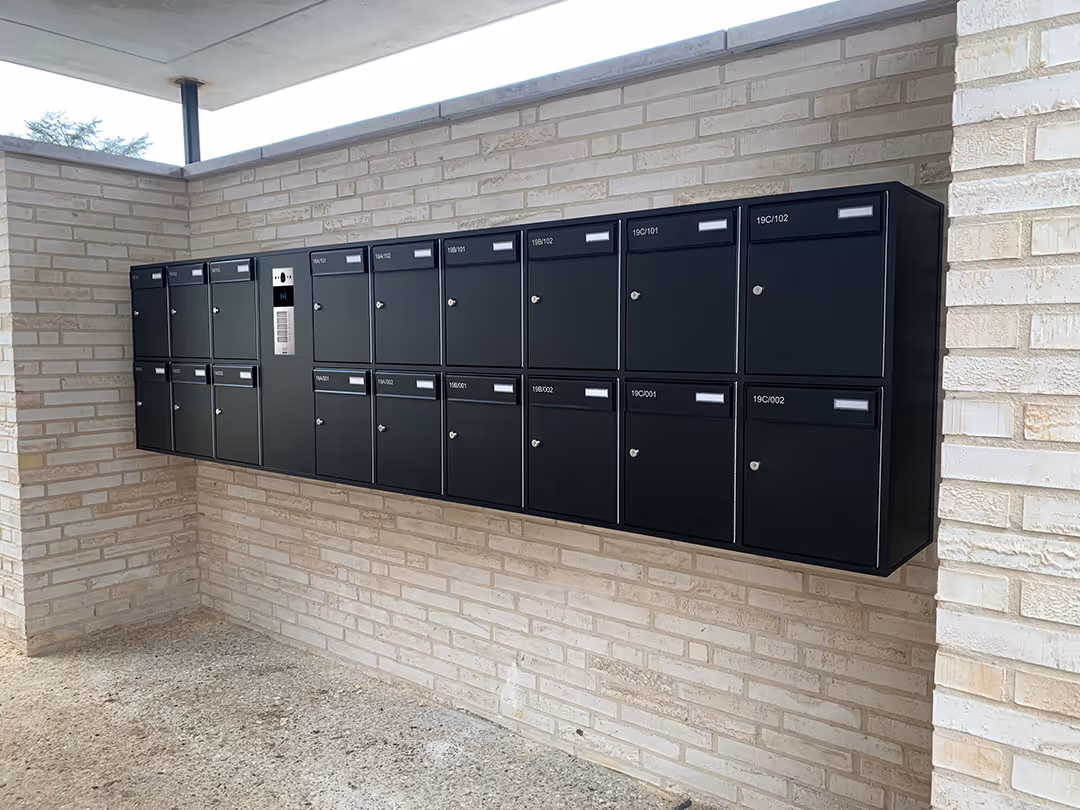 Une grande boîte aux lettres noire fixée à un mur en briques.