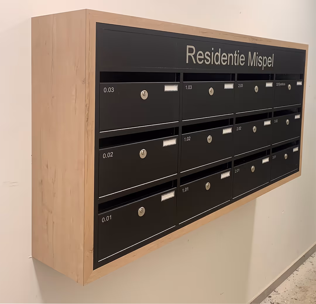 Une boîte aux lettres noire avec un cadre en bois contre un mur blanc.