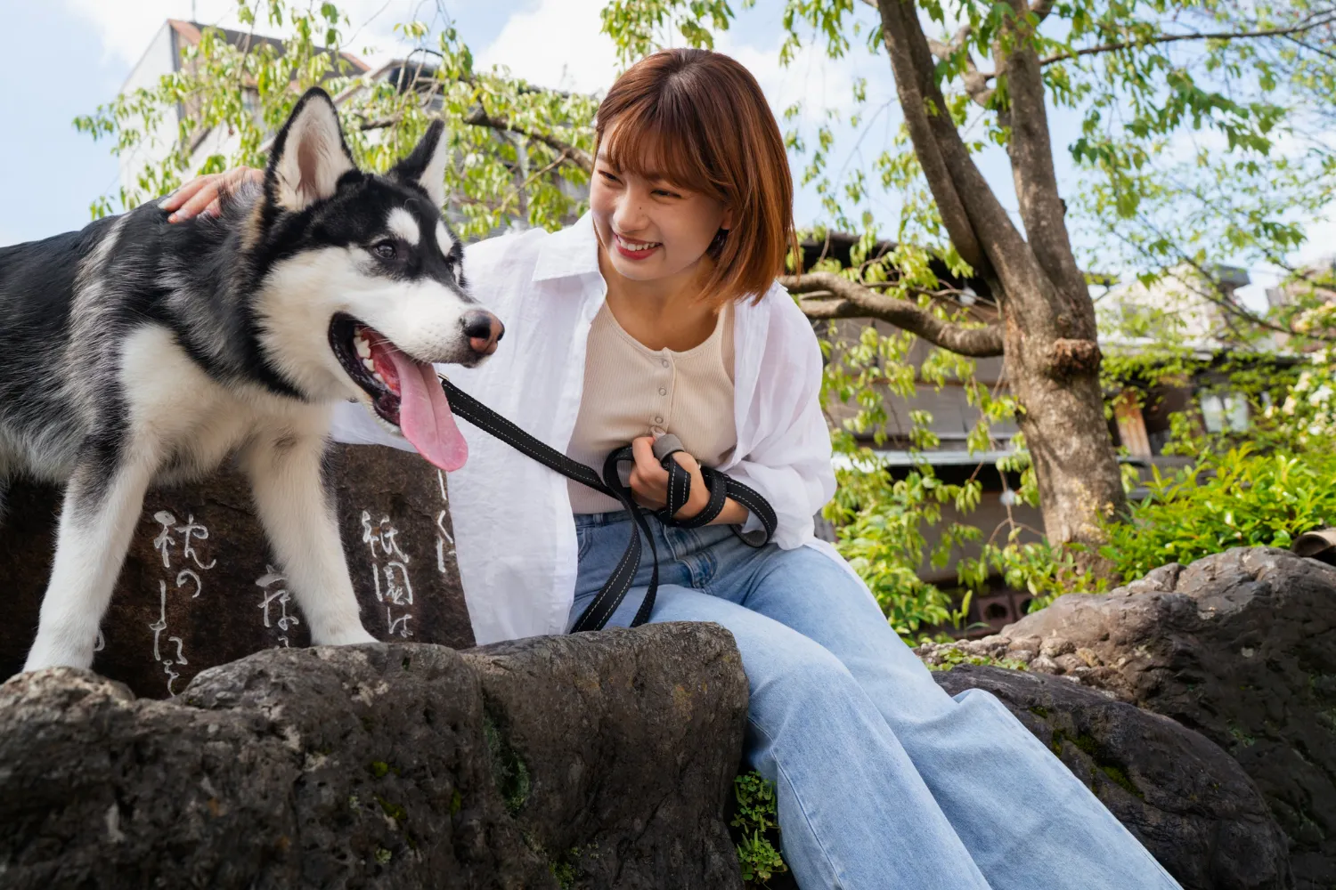 A woman sitting on a rock with a dog on a leash.