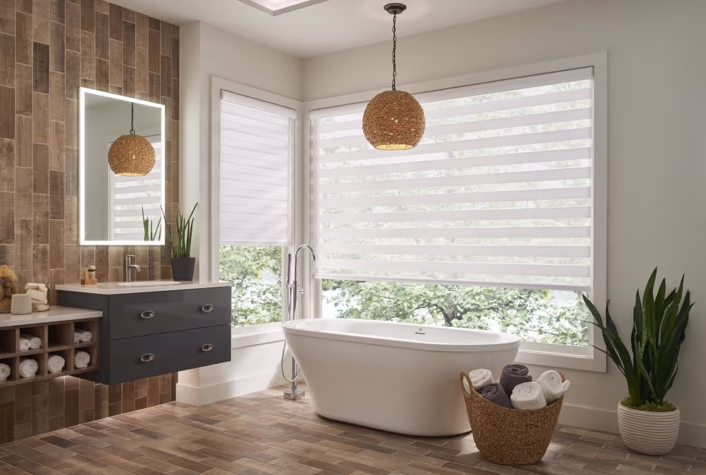 Modern bathroom with large windows featuring light-filtering zebra shades from Cali Coast Shutters & Shades, styled with a freestanding tub, wood accents, and natural lighting