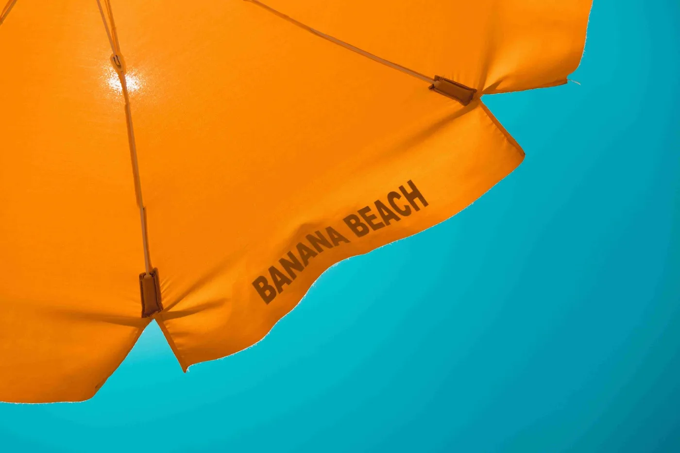 Ein orangefarbener Sonnenschirm mit der Aufschrift "BANANA BEACH" vor einem klaren, blauen Himmel. Die Farben sind lebhaft und vermitteln ein Gefühl von Sommer und Entspannung, ideal für die Präsentation einer Ferienwohnung bei Ferienvermietungen und kurzfristigen Vermietungen.
