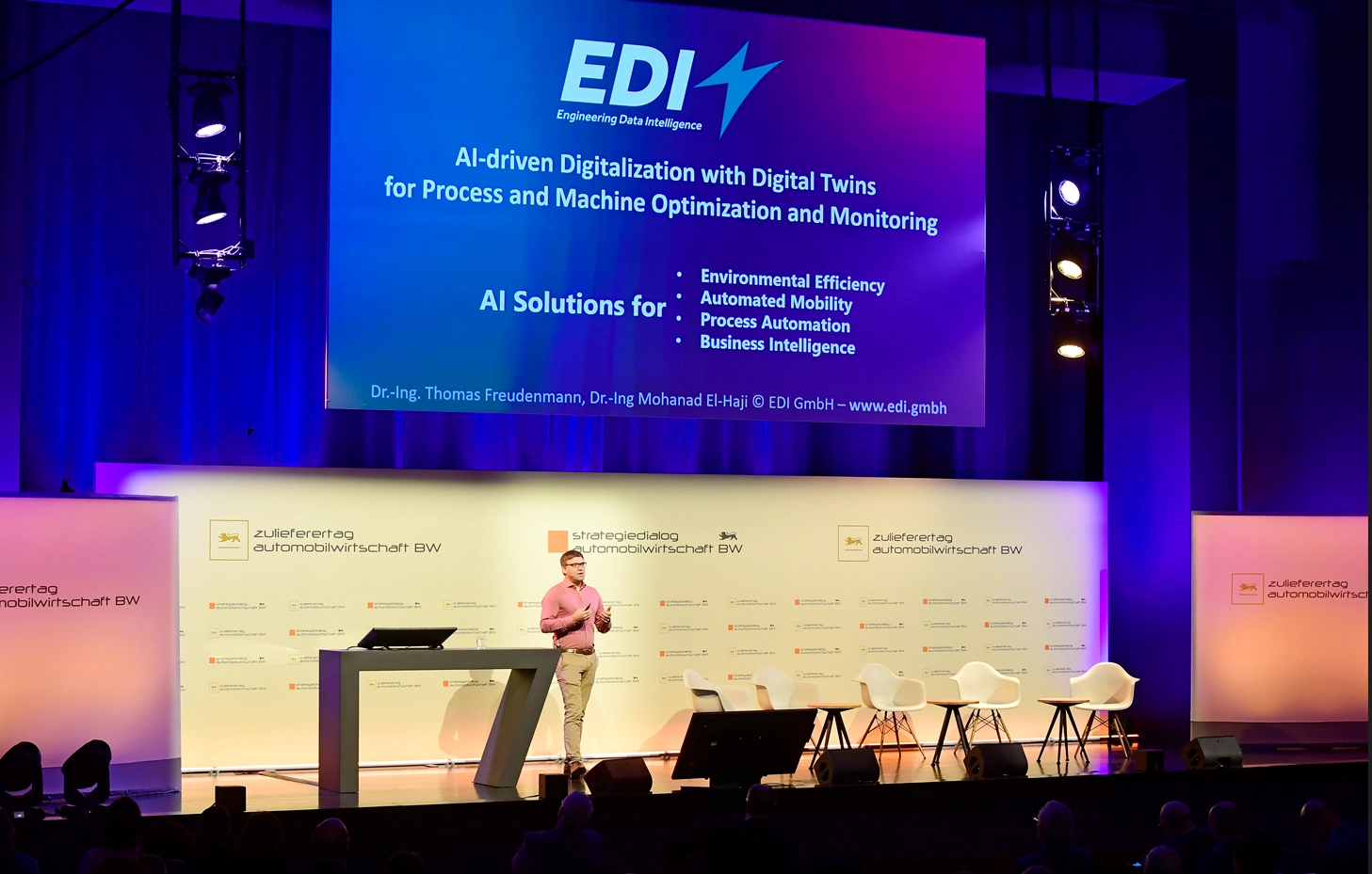 Thomas Freudenmann presenting on stage with a screen displaying EDI's AI and Digital Twin solutions.