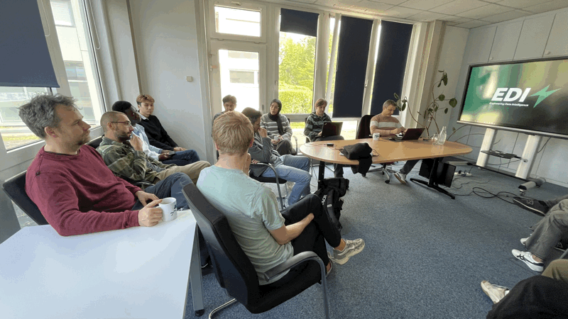 Several EDI GmbH team members are seated in a modern meeting room, attending a presentation with a large screen displaying the 'EDI!' logo.