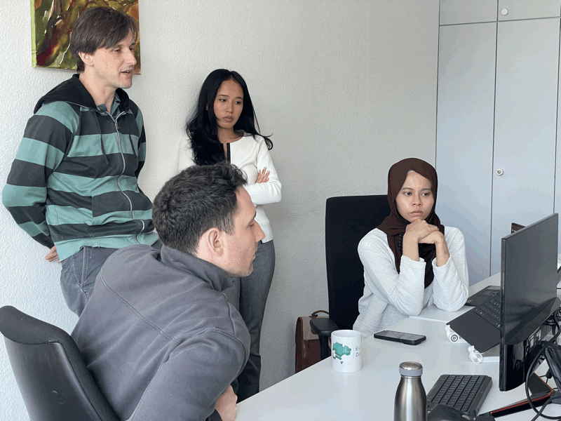 Three EDI GmbH team members, two men and one woman, collaboratively work together around a computer screen in an office setting.