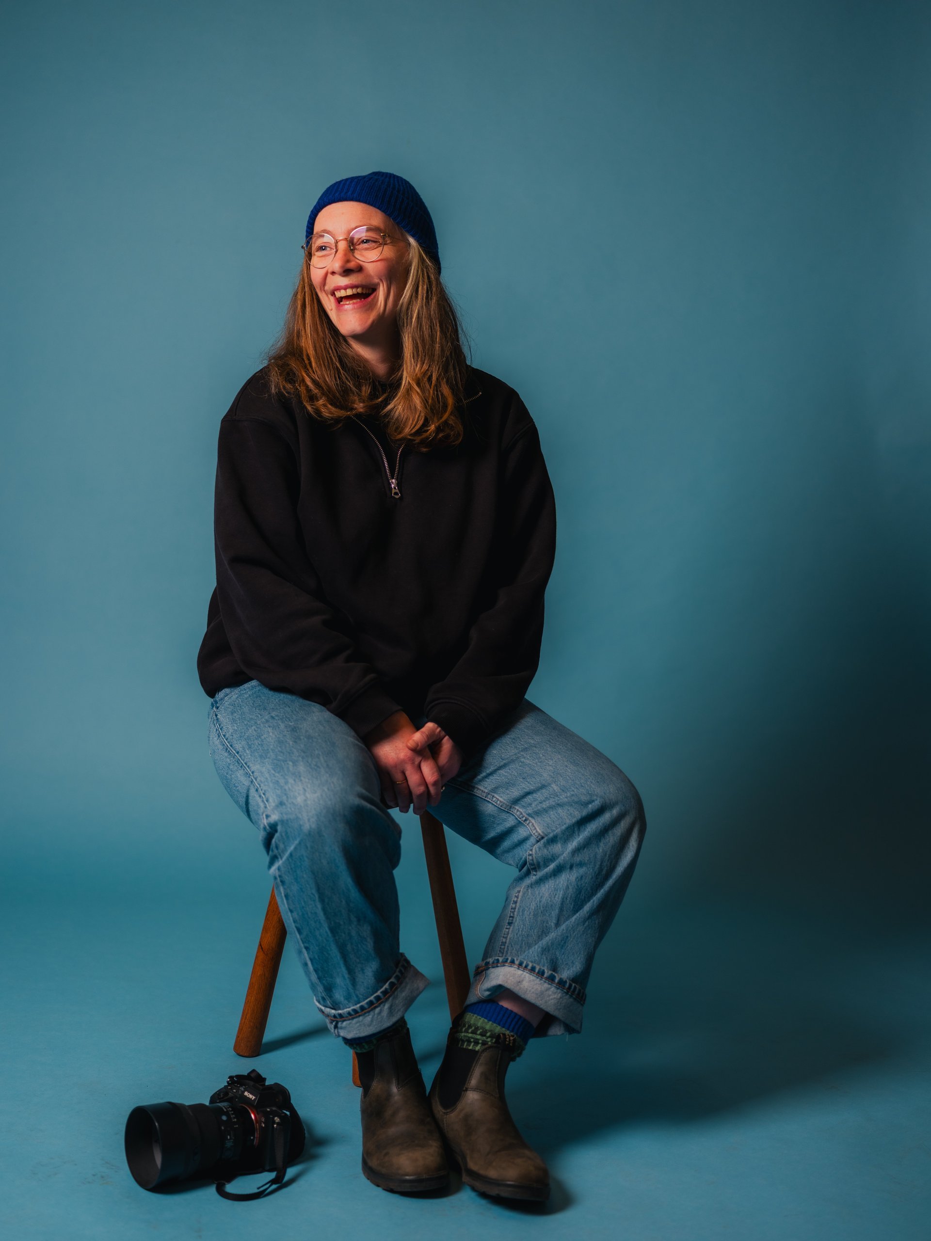 Liesbet De Waele laughing on a stool in her studio, camera at her feet