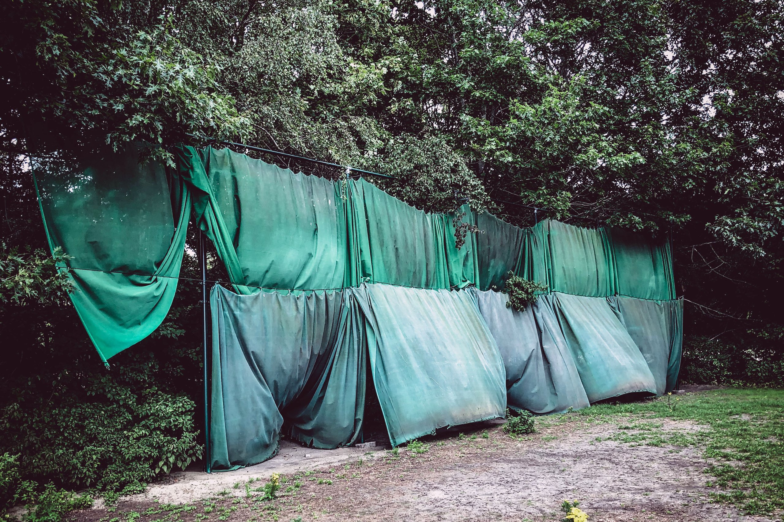 Green tarpaulin curtains draped between the trees at the Blaarmeersen, Ghent