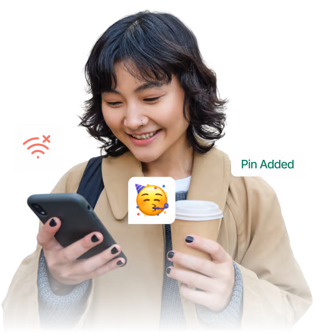 Smiling woman in a beige coat holding a coffee cup in one hand and a smartphone in the other.