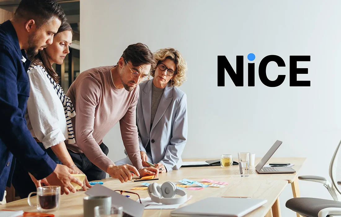 A photo of people working together while looking at papers in a conference room and the NiCE logo in the upper corner of the photo