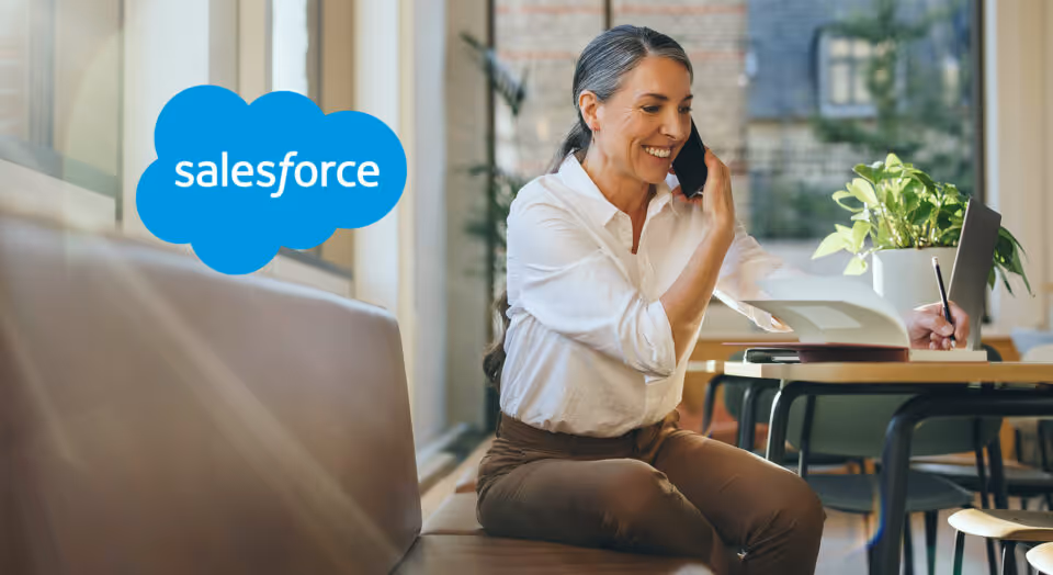 A photo of a woman talking on a cell phone and writing with her other hand with the Salesforce logo in the upper corner of the photo
