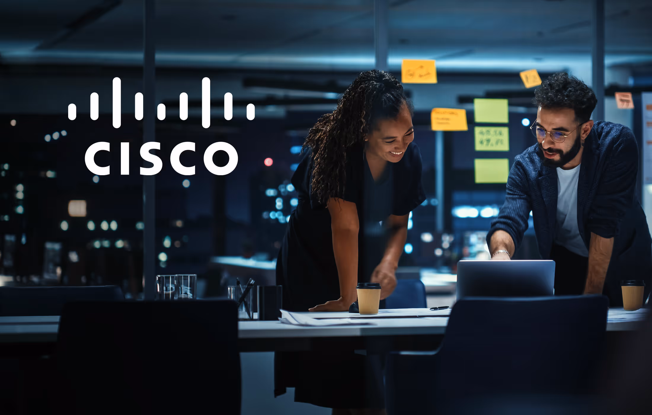 A man and woman looking at a laptop together in an office with the Cisco logo in the upper corner of the photo