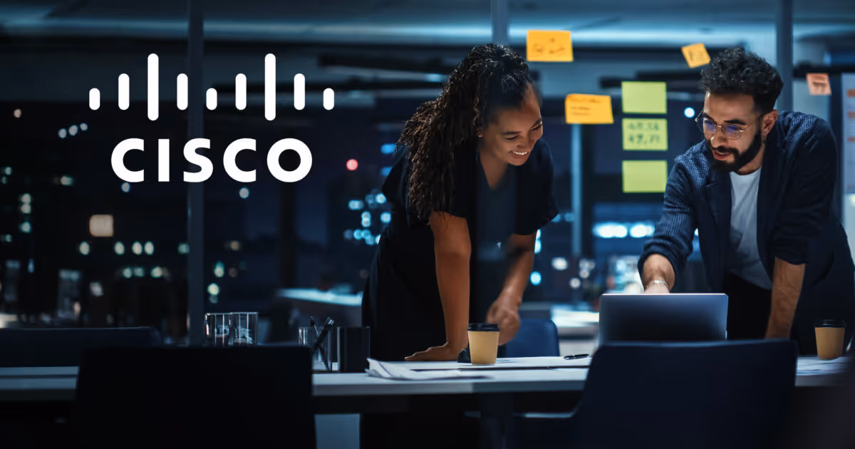 A man and woman looking at a laptop together in an office with the Cisco logo in the upper corner of the photo