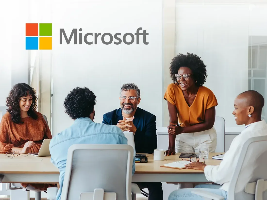 A phone of workers gathered around a conference room table with the Microsoft logo in the upper corner of the photo
