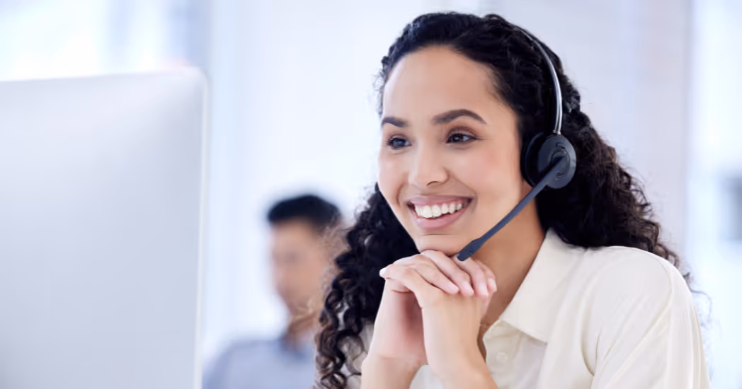 A smiling contact center agent looks at her computer screen while wearing a headset.