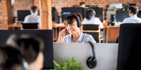 A contact center agent smiles while sitting at her computer with a headset on.