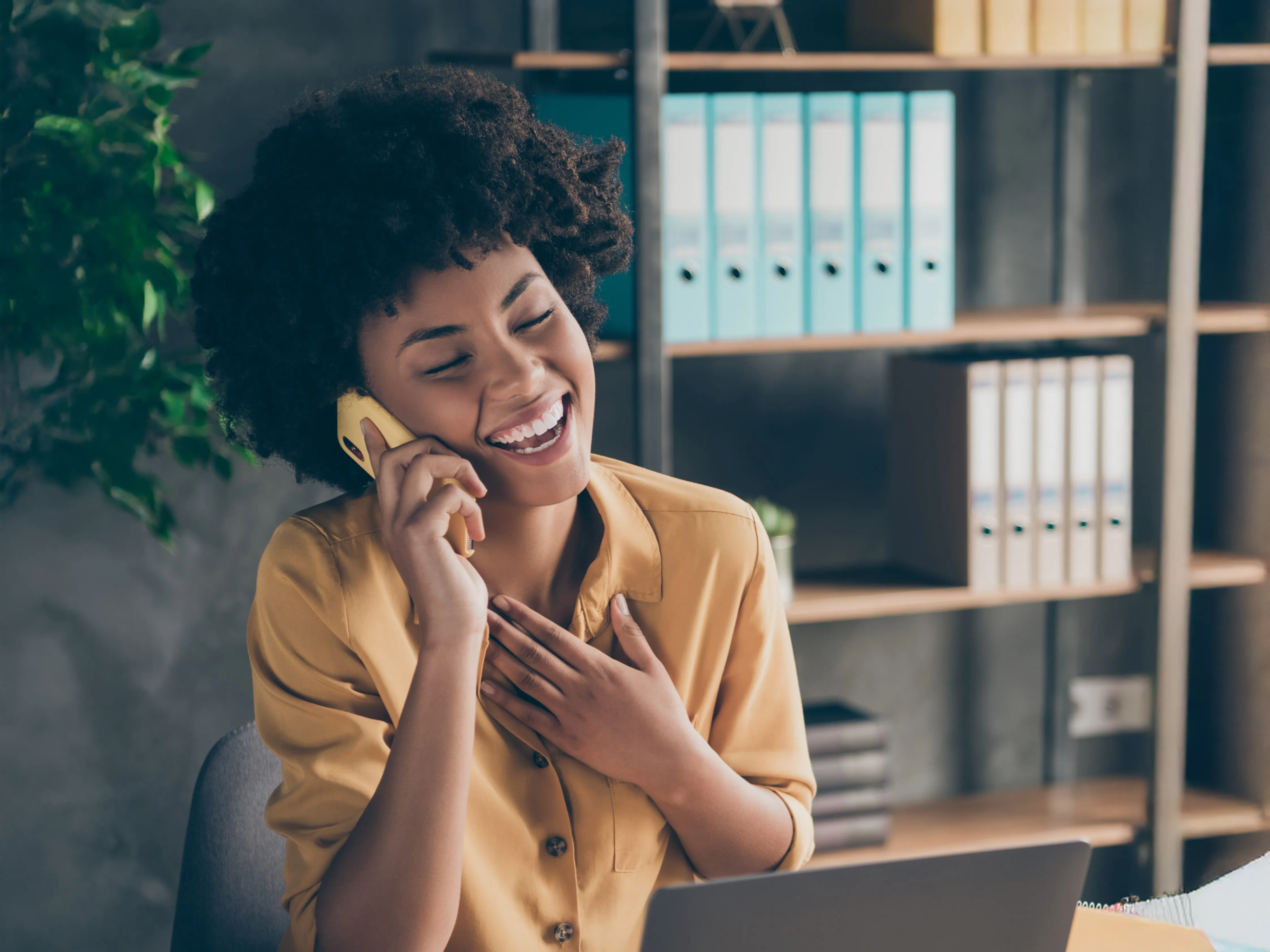 A woman laughs while talking on a yellow cell phone.