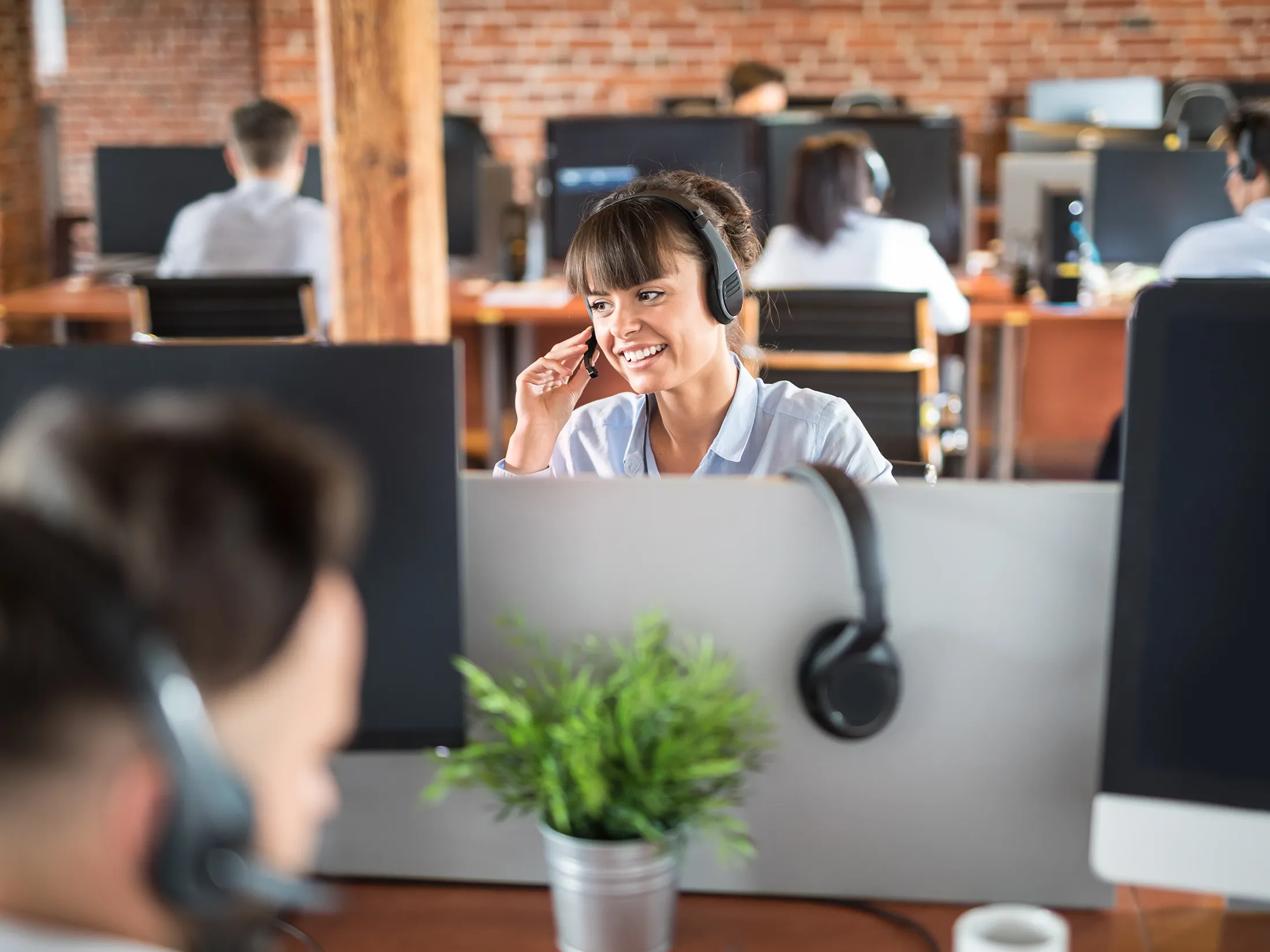 A woman smiles while talking through her agent headset in a busy office.